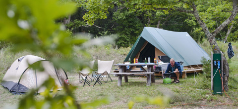 Campingområde med telt, picnicbord og en person, der laver mad ved Bonaventure-teltet i Sud-Ardèche, Frankrig.