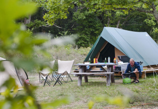 Campingområde med telt, picnicbord og en person, der laver mad ved Bonaventure-teltet i Sud-Ardèche, Frankrig.