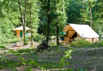 Safari-Zelt Canadienne im Village Huttopia Senonches, Frankreich, zwischen hohen, grünen Bäumen.