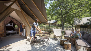 Familie geniet van buitenleven aan een Trappeur safaritent met houten terras in een groen dorp.