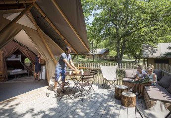 Famiglia si rilassa in una tenda safari Trappeur con terrazza di legno immersa nella natura del villaggio.