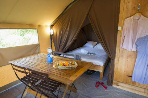 Interieur van een Trappeur tent met houtentafel, fruitmand en bed in Village Huttopia Senonches, Frankrijk.