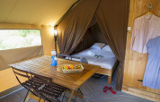 Interior of a Trappeur tent with dining table, fruit basket, and cozy bed at Village Huttopia Senonches, France.