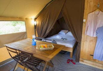 Interno di una tenda Trappeur con tavolo, cesto di frutta e letto nel Village Huttopia Senonches, Francia.