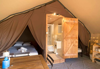 Innenansicht eines Safari-Zelts mit Bett, eigenem Badezimmer mit Dusche und Holzmöbeln im Zelt.