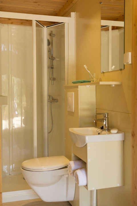Bagno in una tenda safari con box doccia, WC sospeso, piccolo lavandino e specchio a muro.