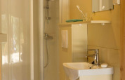 Badezimmer in einem Safarizelt mit Duschkabine, Wandtoilette, kleinem Waschbecken und Spiegel.