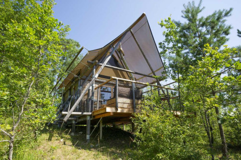 Safari-tent Cahutte in Village Huttopia Senonches, Frankrijk, omgeven door groene bomen en rijke natuur.