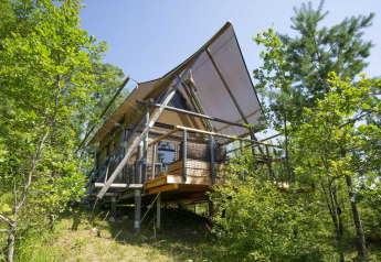 Safari-tent Cahutte in Village Huttopia Senonches, Frankrijk, omgeven door groene bomen en rijke natuur.