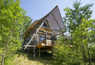 Safari-Zelt Cahutte im Village Huttopia Senonches, Frankreich, eingebettet in grüne Natur mit Bäumen.