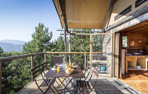 Terraza de madera con mesa y sillas, vista al bosque en una tienda safari en Village Huttopia Senonches, Francia.