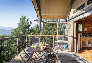 Terraza de madera con mesa y sillas, vista al bosque en una tienda safari en Village Huttopia Senonches, Francia.