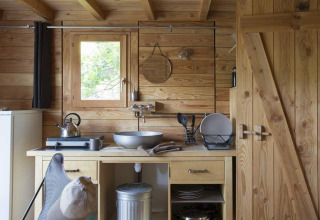 Zona de cocina en la tienda safari Cahutte en Village Huttopia Senonches, Francia, con paredes de madera.