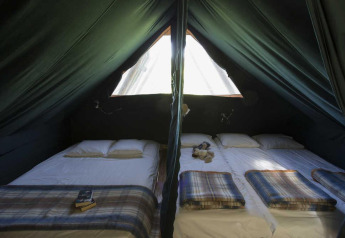 Intérieur d'une tente safari Cahutte avec deux lits et couvertures au Village Huttopia Senonches, France.