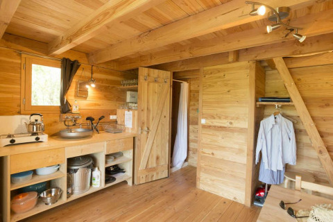 Vista interior de una cabaña de madera con pequeña cocina y zona de estar en Cahutte, Village Huttopia Senonches, Francia.