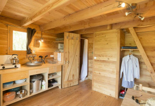 Binnenzicht van een houten hut met keuken en leefruimte in Cahutte, Village Huttopia Senonches, Frankrijk.