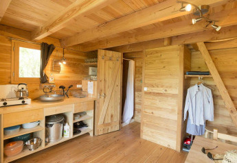 Vista interior de una cabaña de madera con pequeña cocina y zona de estar en Cahutte, Village Huttopia Senonches, Francia.