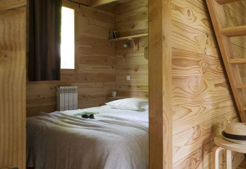 Camera in legno con letto matrimoniale in The cabin at Village Huttopia Senonches, Francia, stile accogliente.