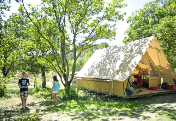Two people enjoy outdoor camping at a spacious Canadienne safari tent nestled under leafy green trees.