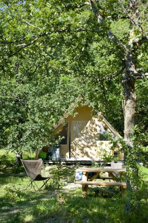 Tienda safari Canadienne en Village Huttopia Dieulefit, Francia, rodeada de árboles y vegetación abundante.