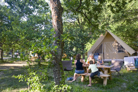 Familie nyder tid ved et picnicbord ved en Canadienne safari-telt på Village Huttopia Dieulefit, Frankrig.