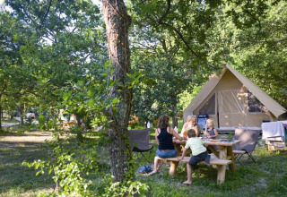 Gezin aan een picknicktafel bij een Canadienne safaritent in Village Huttopia Dieulefit, Frankrijk.
