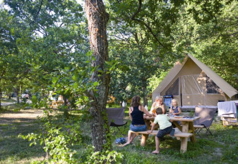 Gezin aan een picknicktafel bij een Canadienne safaritent in Village Huttopia Dieulefit, Frankrijk.