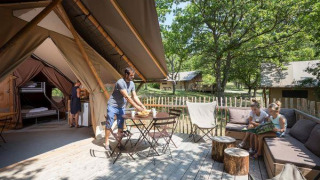Familie geniet op het terras van een Tente Trappeur safaritent, omringd door bomen en natuur.