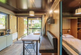 Vista interior de Chalet Evasion en Camping Valkenburg - Maastricht, con mesa, banco y cama.