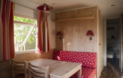 Gemütlicher Innenraum eines Häuschens mit roten Vorhängen und Sitzbank, Camping Valkenburg - Maastricht.