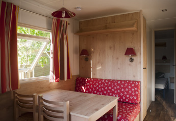 Indretning af en hyggelig hytte med røde gardiner, spisebord og bænk, Camping Valkenburg - Maastricht.