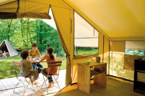 Interno di una tenda safari con persone sedute fuori a un tavolo nei boschi a Huttopia De Roos, Paesi Bassi.