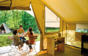 Innenansicht eines Safari-Zelts mit Menschen, die draußen an einem Tisch im Wald bei Huttopia De Roos sitzen.