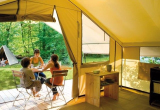 Interior of a safari tent with people sitting outside at a table in the woods at Huttopia De Roos, Netherlands.