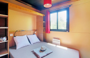 Acogedor dormitorio de cabaña con cama doble, ventana con cortina roja y estantería moderna de madera.