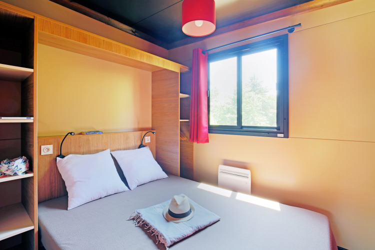 Chambre confortable dans une cabane avec lit double, grande fenêtre, rideau rouge et étagères modernes.