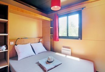 Gemütliches Schlafzimmer in einer Holzhütte mit Doppelbett, Fenster, rotem Vorhang und moderner Ausstattung.