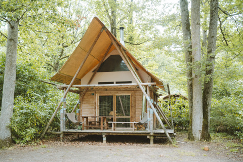 Tienda safari Cahutte en Huttopia De Roos, Países Bajos, rodeada de árboles y naturaleza verde.
