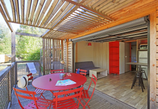 Vista interior y exterior del Chalet Toronto en Huttopia De Roos, Países Bajos, con mesa roja de comedor.