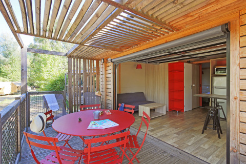 Vista interior y exterior del Chalet Toronto en Huttopia De Roos, Países Bajos, con mesa roja de comedor.