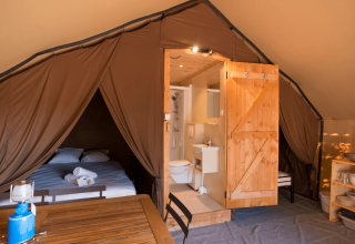 Binnenzicht van Trappeur Tent II op Camping Huttopia De Veluwe met bed, badkamer en eetgedeelte.