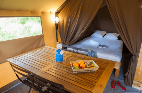 Vista interior de la Trappeur Tent II en Camping Huttopia De Veluwe con cama, mesa y canasta de frutas.