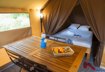 Vue intérieure de la Tente Trappeur II au Camping Huttopia De Veluwe avec lit, table et panier de fruits.