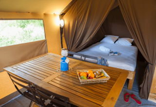 Interior view of Trappeur Tent II at Camping Huttopia De Veluwe featuring a bed, dining table, and fruit.