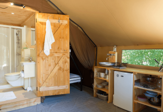 Interior de la Trappeur Tent II con baño, cocina pequeña y ventana en Camping Huttopia De Veluwe, Países Bajos.