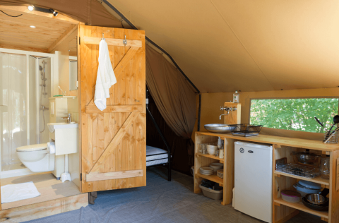 Interiør af Trappeur Tent II med badeværelse, lille køkken og vindue på Camping Huttopia De Veluwe, Holland.