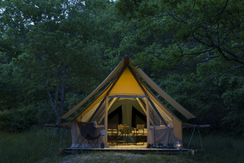 Das Safari-Zelt Canadienne Cosy auf Camping Huttopia De Veluwe in den Niederlanden, beleuchtet im Wald.