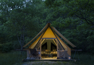 Tenda safari Canadienne Cosy al Camping Huttopia De Veluwe nei Paesi Bassi, illuminata tra gli alberi.
