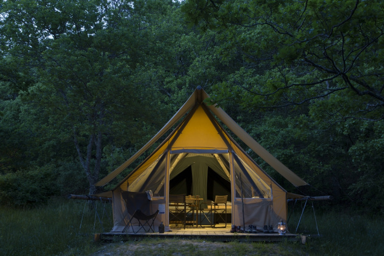 Das Safari-Zelt Canadienne Cosy auf Camping Huttopia De Veluwe in den Niederlanden, beleuchtet im Wald.