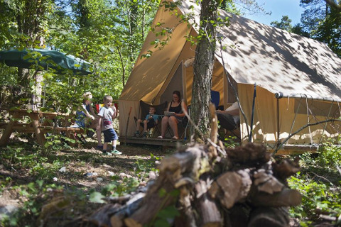 Family camping in front of a Canadienne safari tent at Village Huttopia Lanmary, France, surrounded by trees.
